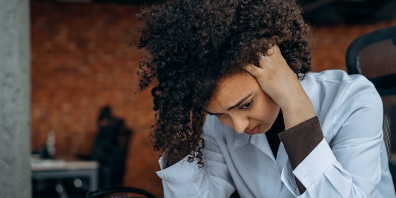 Distressed black woman with her head in her hands feeling overwhelmed at work.